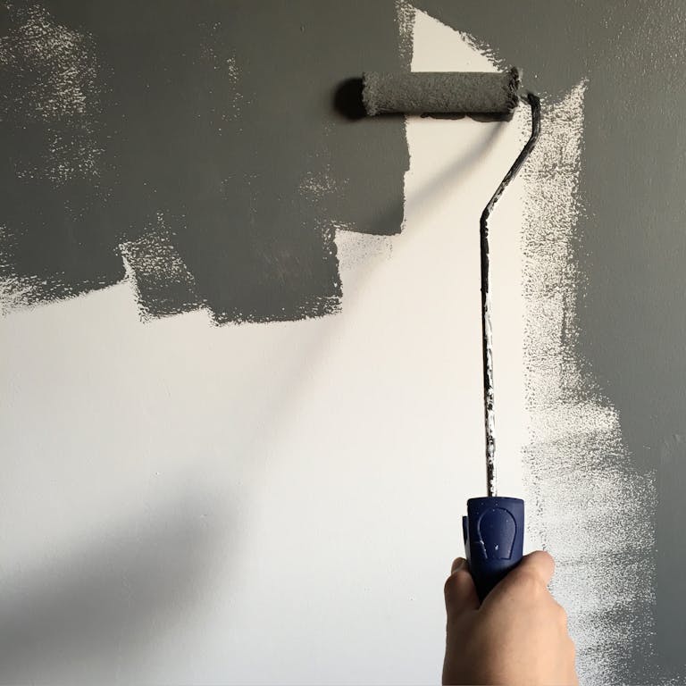 A hand painting a wall gray with a roller during a house renovation project showing the need to update, renovate, and that includes a voice update.