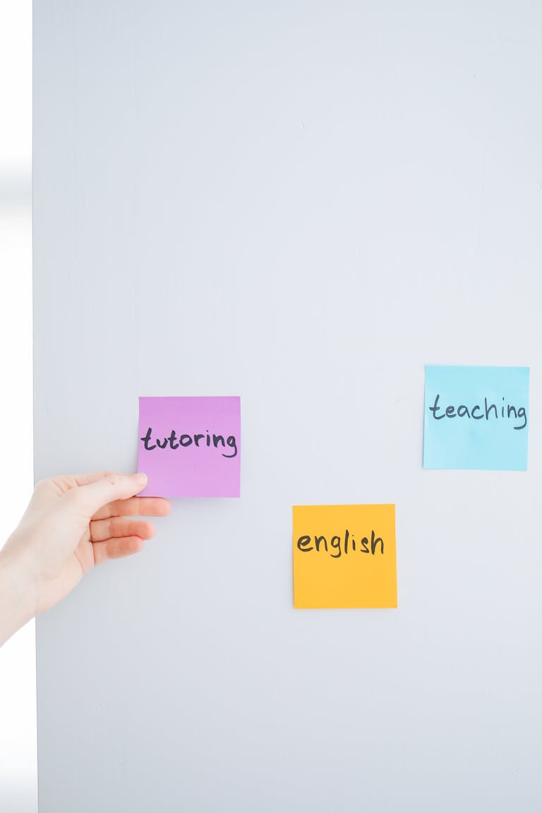 Hand placing sticky notes with words tutoring, teaching, and English on a wall, ideal for educational content.
