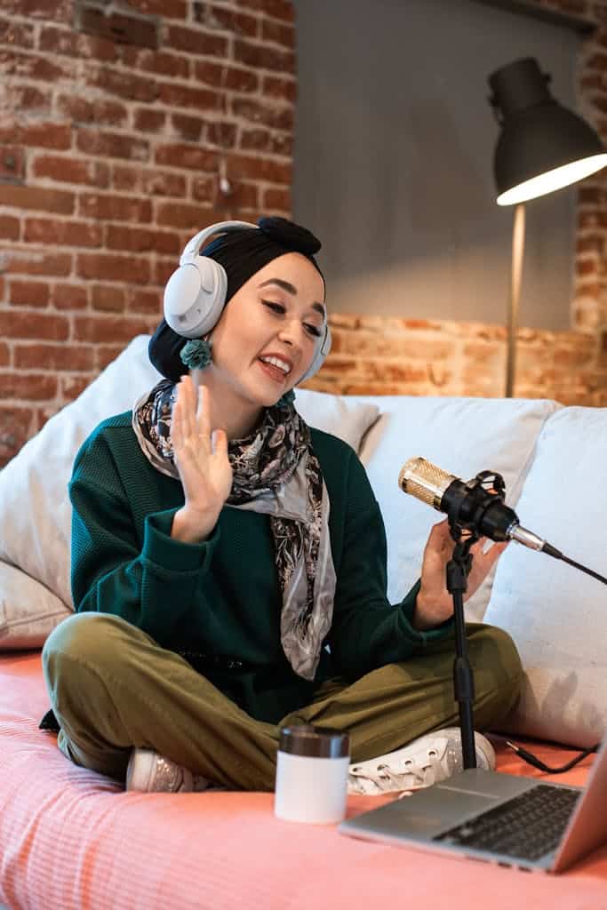 Young woman wearing headphones recording a podcast at home with a microphone.