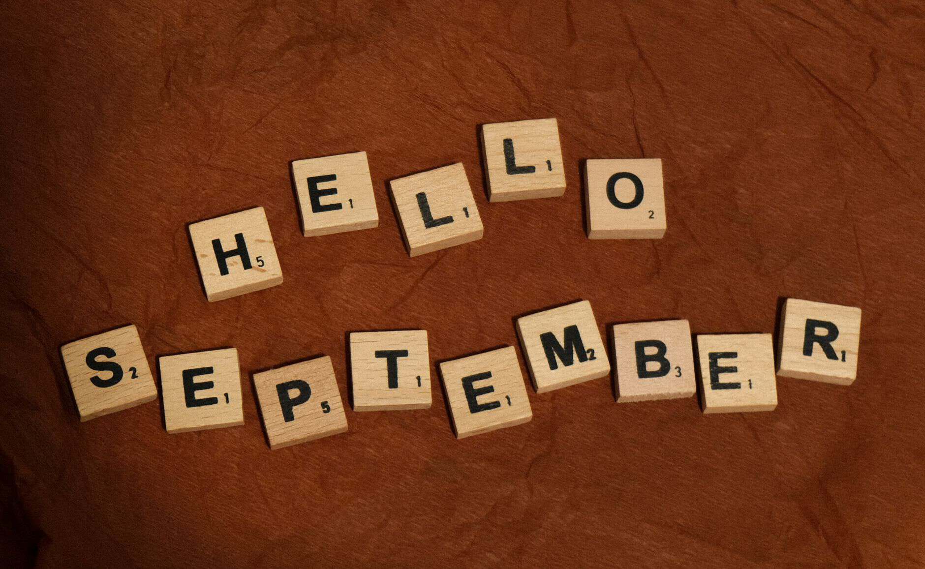 hello september written in scrabble letters on brown paper